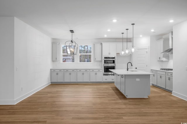 kitchen featuring pendant lighting, sink, wall chimney exhaust hood, and a center island with sink