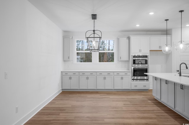 kitchen featuring sink, white cabinetry, double oven, decorative light fixtures, and light wood-type flooring