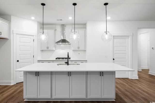 kitchen with an island with sink, decorative light fixtures, and wall chimney exhaust hood