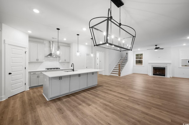 kitchen featuring sink, wall chimney range hood, hanging light fixtures, an island with sink, and stainless steel gas cooktop