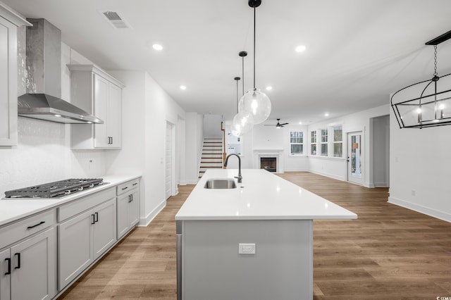 kitchen featuring an island with sink, sink, hanging light fixtures, stainless steel gas cooktop, and wall chimney range hood