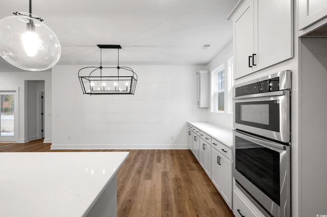 kitchen featuring white cabinetry, light stone counters, decorative light fixtures, double oven, and hardwood / wood-style flooring