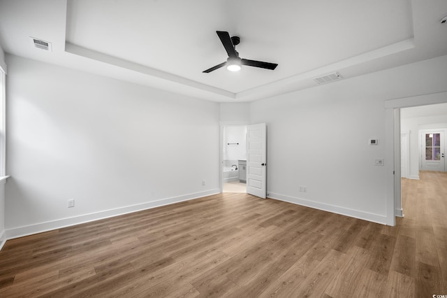 unfurnished bedroom featuring ceiling fan, hardwood / wood-style floors, ensuite bath, and a tray ceiling