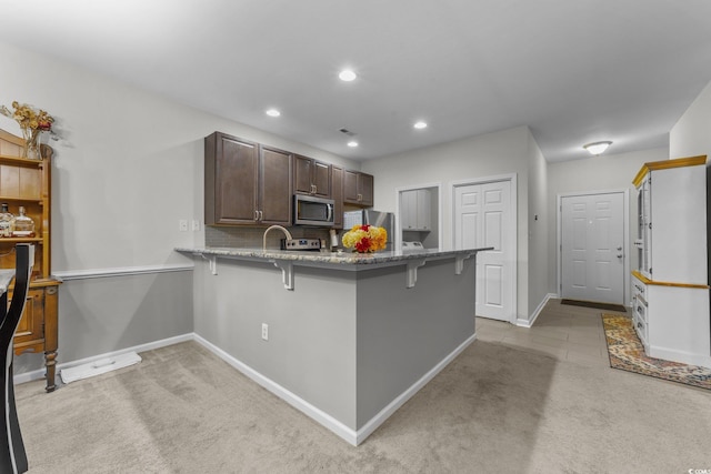 kitchen featuring kitchen peninsula, appliances with stainless steel finishes, dark brown cabinetry, light colored carpet, and a breakfast bar area