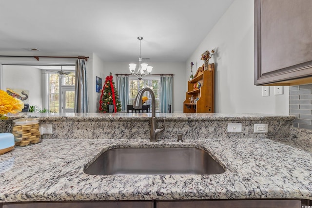 kitchen featuring light stone countertops, sink, hanging light fixtures, and a notable chandelier