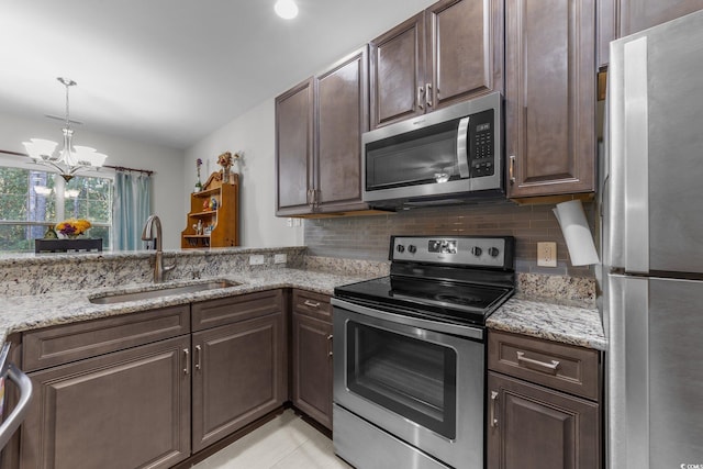 kitchen featuring appliances with stainless steel finishes, light stone counters, dark brown cabinetry, sink, and a chandelier