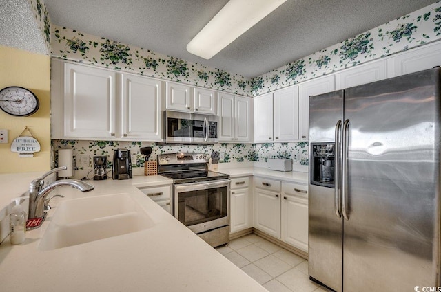 kitchen featuring a textured ceiling, stainless steel appliances, sink, light tile patterned floors, and white cabinetry