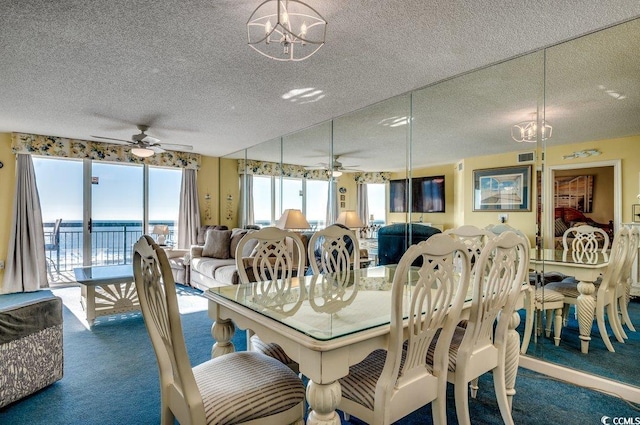 dining area with a textured ceiling, ceiling fan with notable chandelier, a water view, and dark carpet