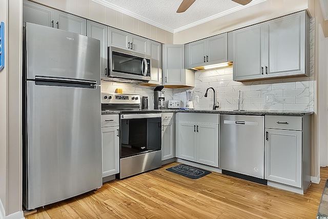 kitchen featuring light wood-type flooring, ornamental molding, stainless steel appliances, ceiling fan, and sink