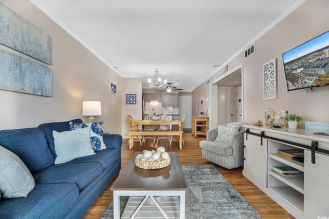 living room with wood-type flooring, crown molding, and an inviting chandelier