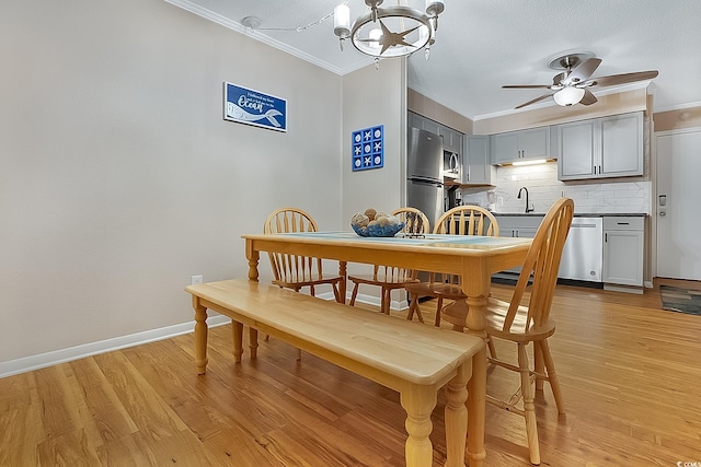 dining area with ceiling fan with notable chandelier, light wood-type flooring, crown molding, and sink