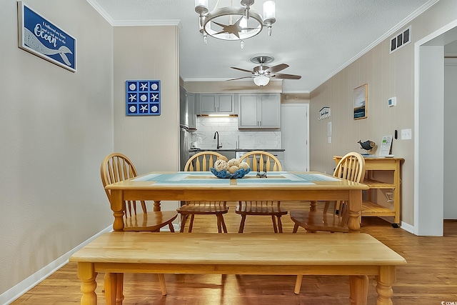 dining space with a textured ceiling, crown molding, light hardwood / wood-style floors, and ceiling fan with notable chandelier