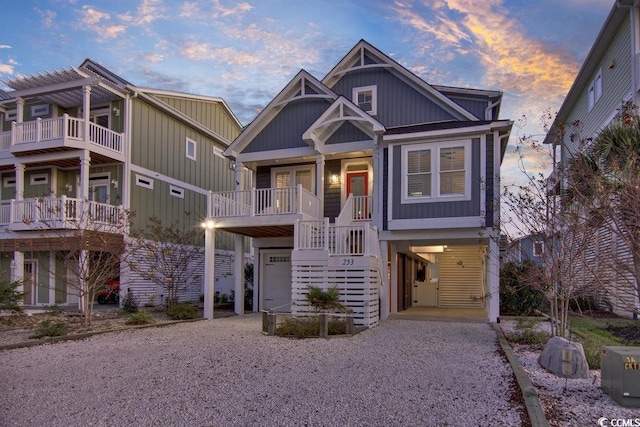 craftsman-style house with a carport, covered porch, stairway, board and batten siding, and gravel driveway