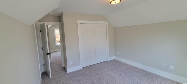 unfurnished bedroom featuring a closet, light colored carpet, and vaulted ceiling