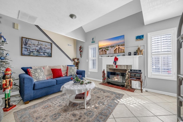 living room with a textured ceiling, a brick fireplace, vaulted ceiling, and light tile patterned flooring