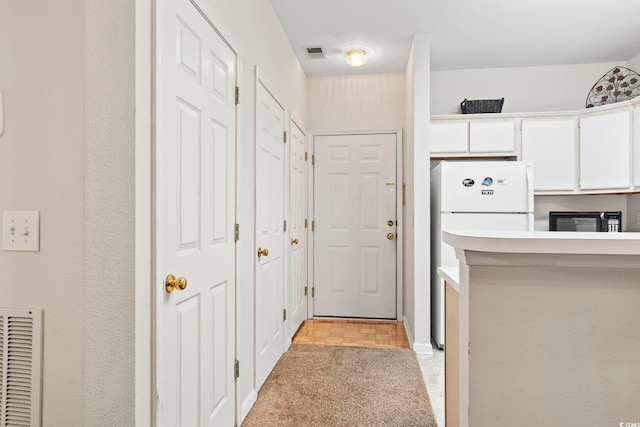 kitchen featuring white cabinetry, white fridge, and light colored carpet