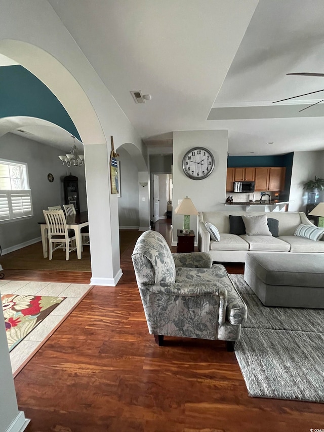 living room featuring dark wood-type flooring and ceiling fan with notable chandelier