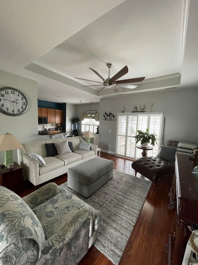 living room with ceiling fan, ornamental molding, dark wood-type flooring, and a tray ceiling