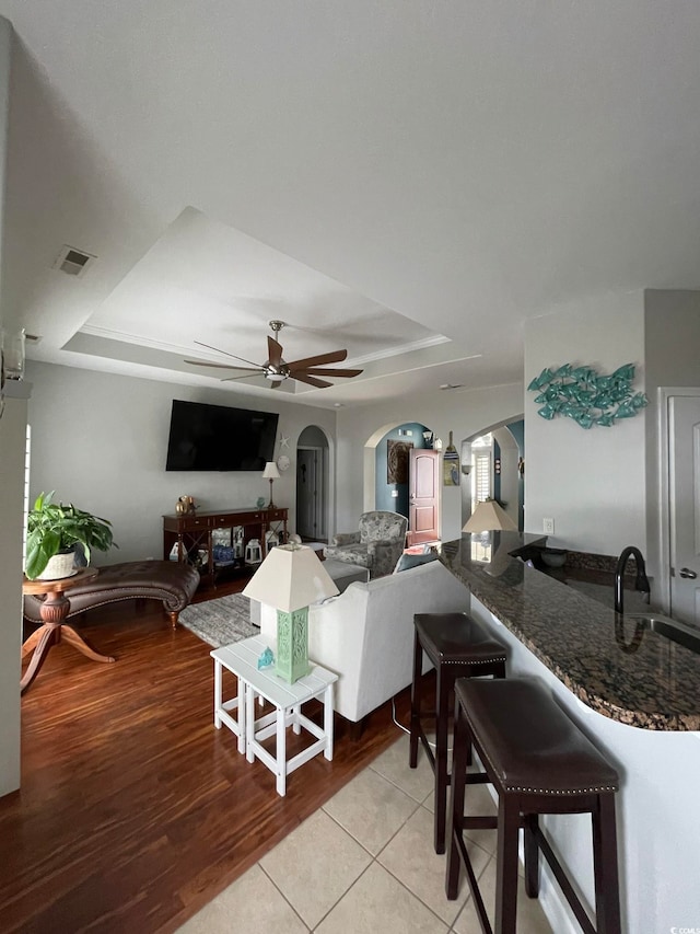 tiled living room featuring a tray ceiling, ceiling fan, and sink