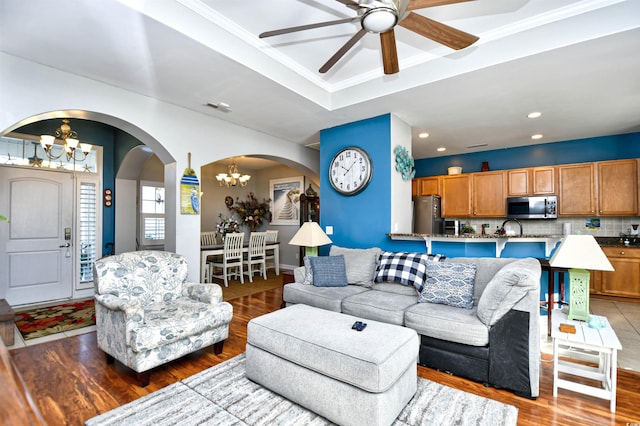 living room featuring sink, a raised ceiling, hardwood / wood-style floors, ceiling fan with notable chandelier, and ornamental molding