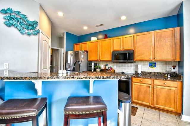 kitchen with a breakfast bar, stainless steel fridge, dark stone countertops, and decorative backsplash