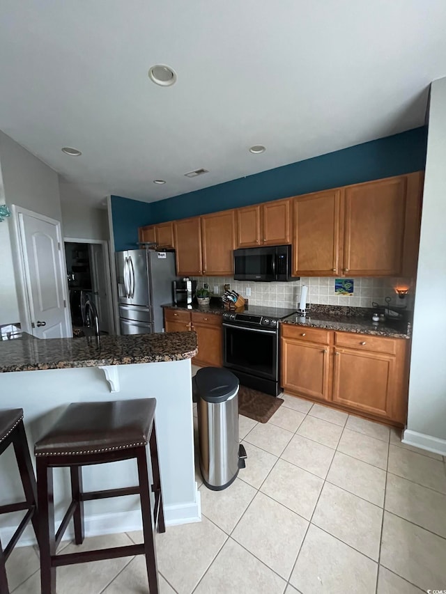 kitchen with decorative backsplash, a breakfast bar, black appliances, light tile patterned floors, and dark stone countertops