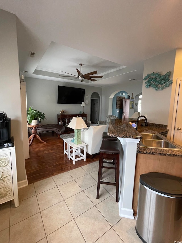 tiled living room featuring a raised ceiling, ceiling fan, and sink