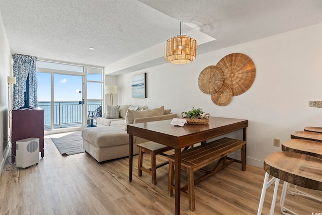 dining space with a textured ceiling, light wood-type flooring, a water view, and a wall of windows