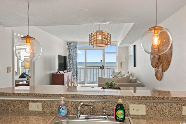 kitchen featuring a textured ceiling, light stone counters, sink, and decorative light fixtures