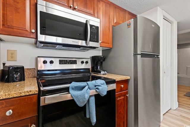 kitchen featuring a textured ceiling, light hardwood / wood-style floors, light stone countertops, and stainless steel appliances