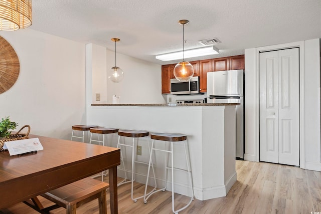 kitchen with kitchen peninsula, pendant lighting, stainless steel appliances, and light wood-type flooring