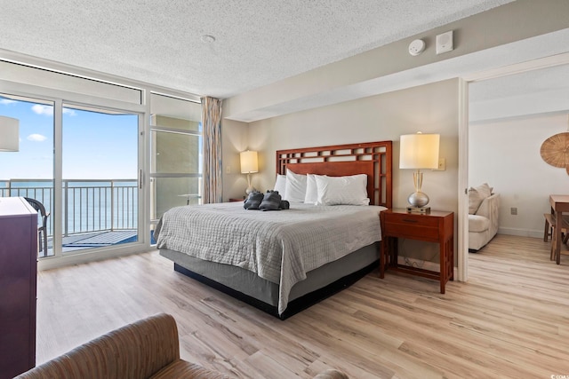 bedroom featuring a water view, light wood-type flooring, a textured ceiling, and access to outside