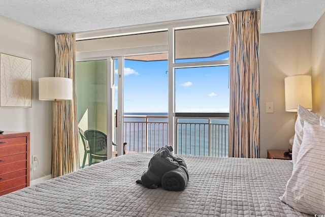 bedroom with access to outside, multiple windows, a water view, and a textured ceiling