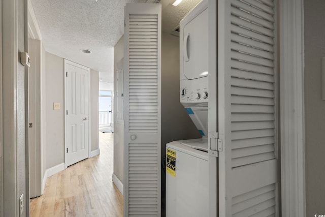 clothes washing area with a textured ceiling, light hardwood / wood-style flooring, and stacked washer / dryer