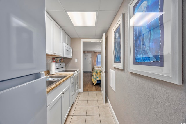 kitchen with a paneled ceiling, white cabinets, white appliances, and light tile patterned floors