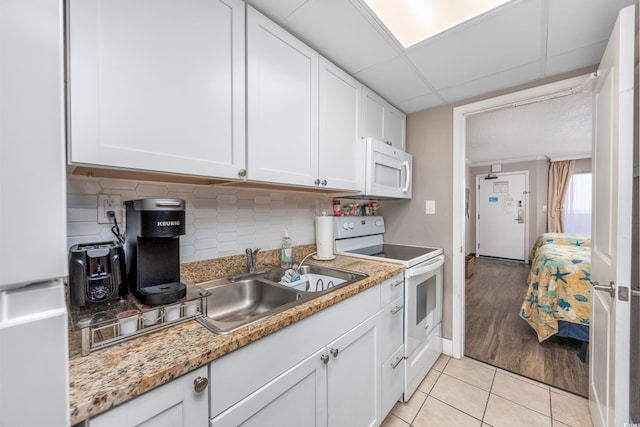 kitchen with white appliances, backsplash, white cabinets, sink, and light tile patterned floors