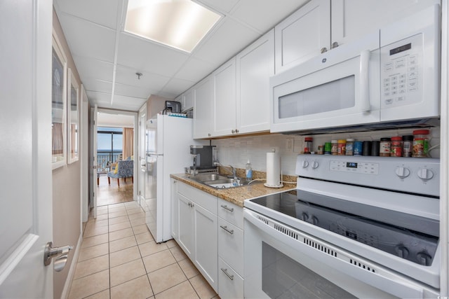 kitchen with white appliances, white cabinets, sink, light tile patterned floors, and tasteful backsplash