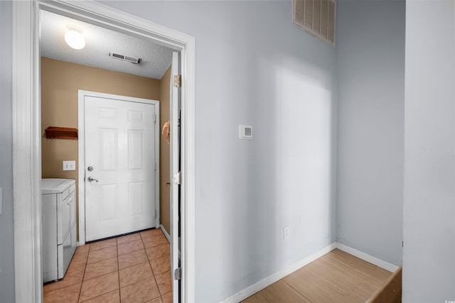 doorway with washing machine and dryer, light tile patterned floors, and a textured ceiling