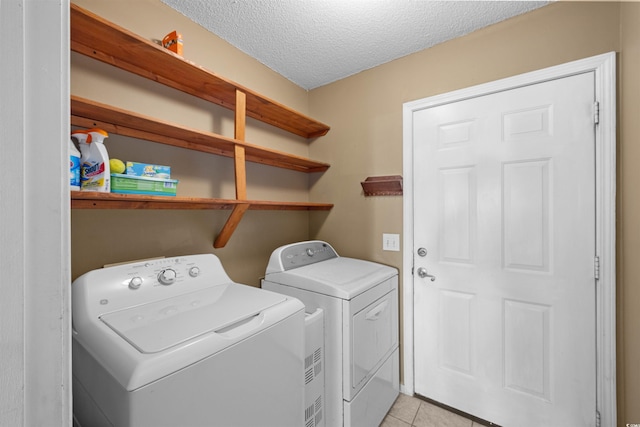 clothes washing area featuring light tile patterned floors, washer and dryer, and a textured ceiling