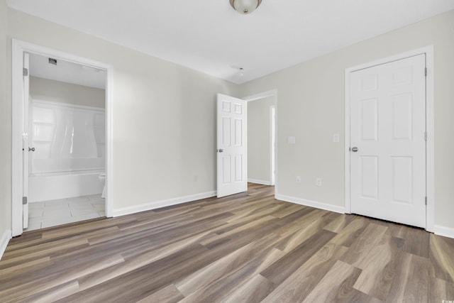 unfurnished bedroom with ensuite bathroom and dark hardwood / wood-style floors