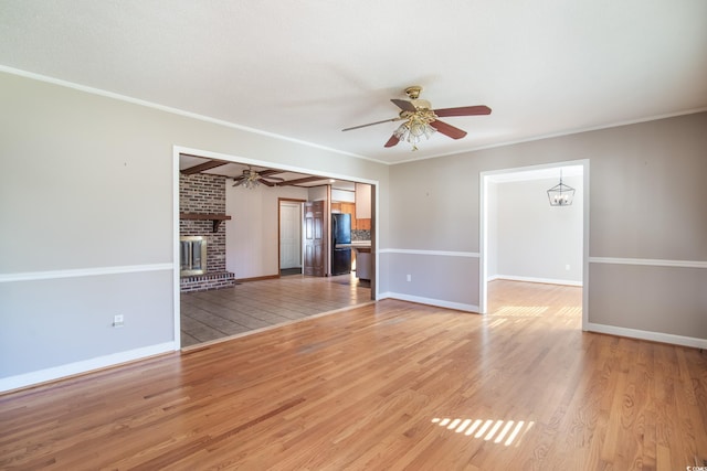 unfurnished living room with ceiling fan with notable chandelier, light hardwood / wood-style floors, a brick fireplace, and crown molding