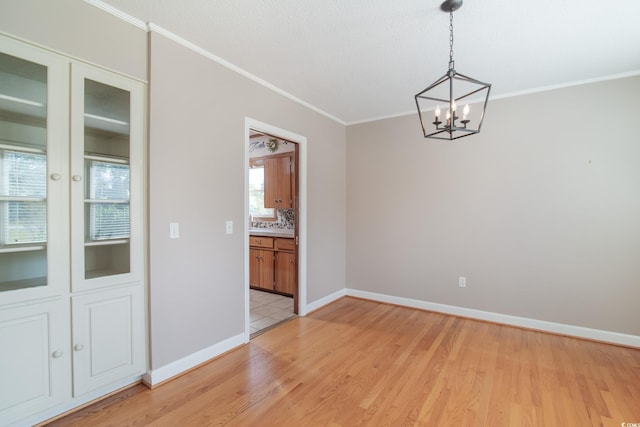 unfurnished dining area featuring an inviting chandelier, crown molding, and light hardwood / wood-style flooring