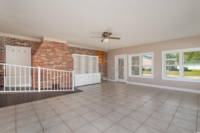 unfurnished room with ceiling fan, light tile patterned flooring, and brick wall