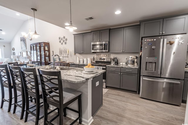 kitchen featuring light stone countertops, stainless steel appliances, sink, pendant lighting, and a breakfast bar area