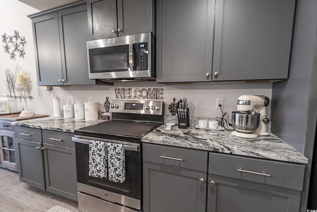 kitchen featuring light hardwood / wood-style flooring, stainless steel appliances, gray cabinets, and light stone counters