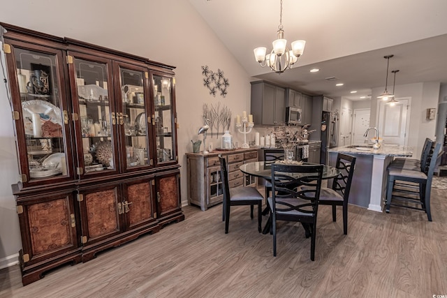 dining room featuring light wood-type flooring, lofted ceiling, sink, and a chandelier