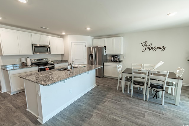 kitchen with white cabinets, hardwood / wood-style floors, stainless steel appliances, and an island with sink