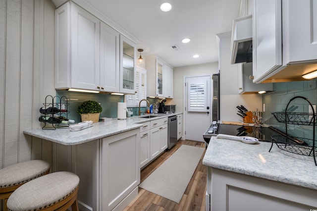 kitchen with appliances with stainless steel finishes, light stone counters, sink, white cabinets, and a breakfast bar area