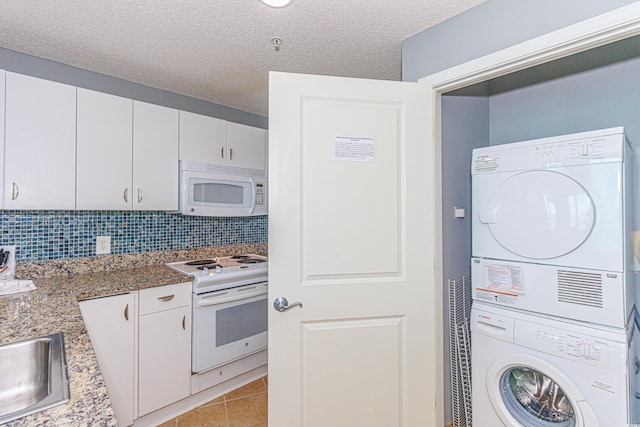 kitchen with stacked washer / drying machine, white cabinetry, white appliances, and dark stone counters