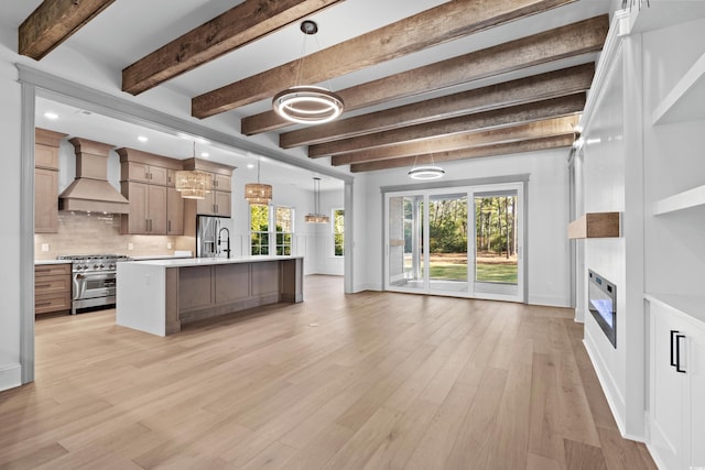 kitchen featuring appliances with stainless steel finishes, backsplash, a kitchen island with sink, hanging light fixtures, and custom range hood